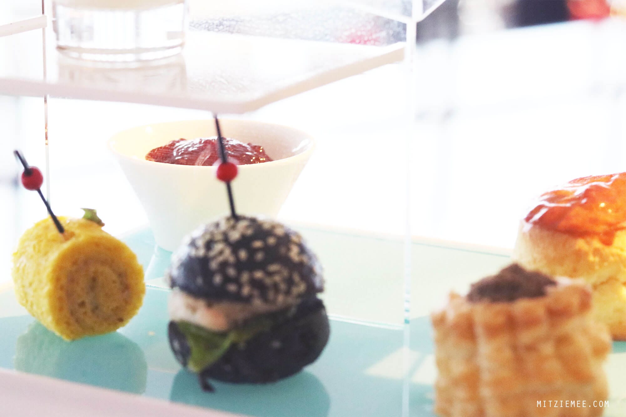  On my last day in Hong Kong it was pouring down. I had to check out from the hotel at noon, but my flight was not until the evening, and my original plan to go for a walk along the water did not seem very attractive. Instead I called The Ritz-Carlton in Hong Kong and made a reservation for the afternoon tea at Café 103. My table was far from the floor-to-ceiling windows, so even though I was on the 103rd floor, I did not have much of a view. Instead they provided me with different kinds of magazine, so I wouldn’t get bored during my afternoon tea for one. Except for the view (or the lack of it), it was a really nice afternoon tea. First, I was asked to pick the tea I wanted, and it was more difficult than it sounds, because there were so many different kinds to choose among. After consulting the waiter, who turned out to be very well-versed in teas, I finally decided on the Sakura Sakura tea, which was a green tea with cherry blossoms and a mild and flowery flavor. The Ritz-Carlton in Hong Kong are known for collaborations with chefs and different gourmet brands for the afternoon tea, and when I was there, the menu was made in collaboration with luxury candy store Sugarfina, which are particularly known for boozy gummy bears. One of the desserts I had was a champagne cream with strawberry topped with a champagne-infused gummy bear, and it was exquisite. I could have eaten a whole family of those bears:) It was a nice way to spend the afternoon but next time I go, I will try to get a table with a better view. I did a little online research, and it seems like The Lounge & Bar, which is on the 102nd floor and also serves afternoon tea, has more window tables available, so maybe they are a better choice. Otherwise, there is always Ozone, which is the beautiful bar on the 118th floor at the Ritz-Carlton. 